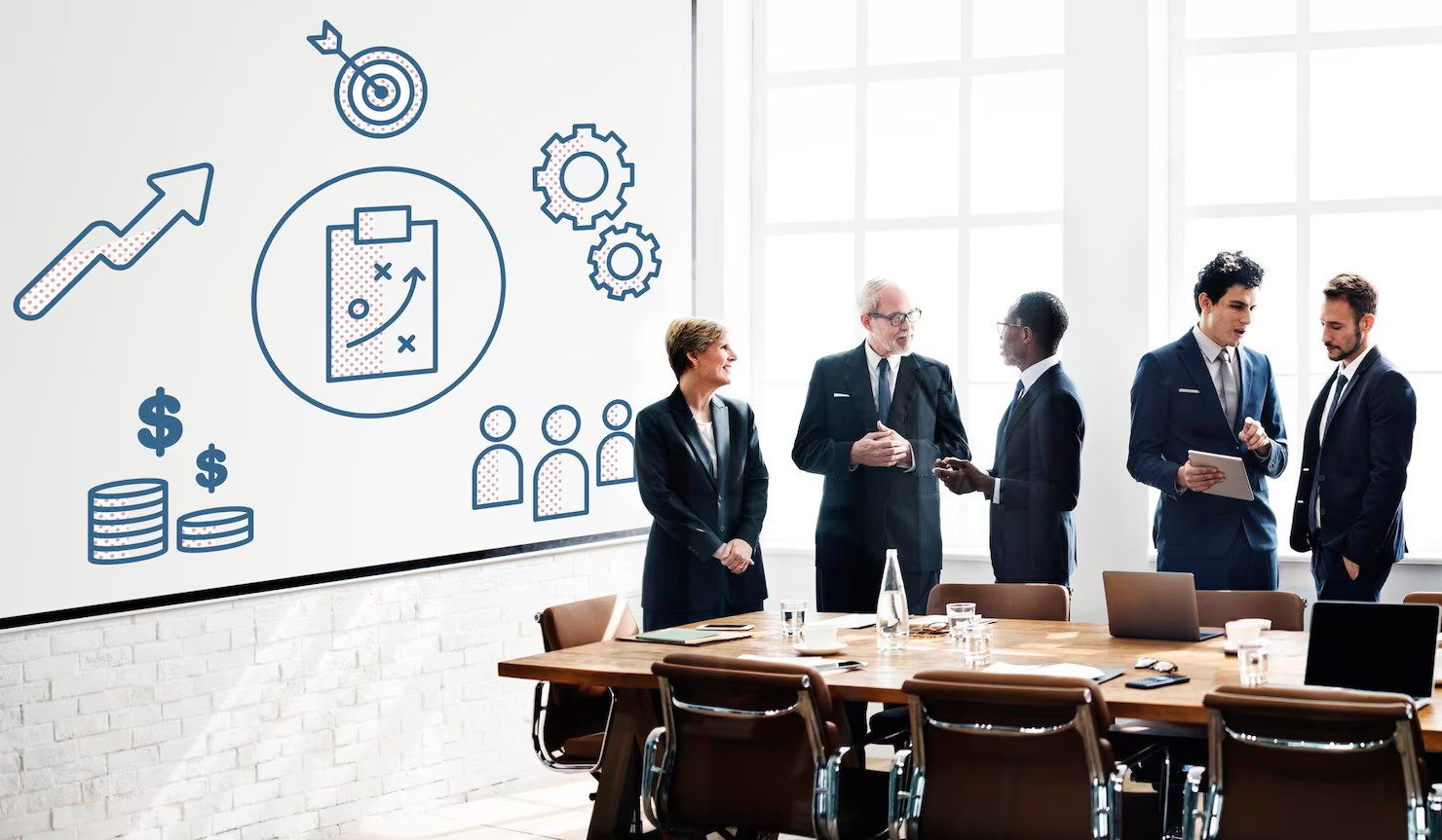 Business leaders discuss strategy beside a presentation of goals and business processes.
