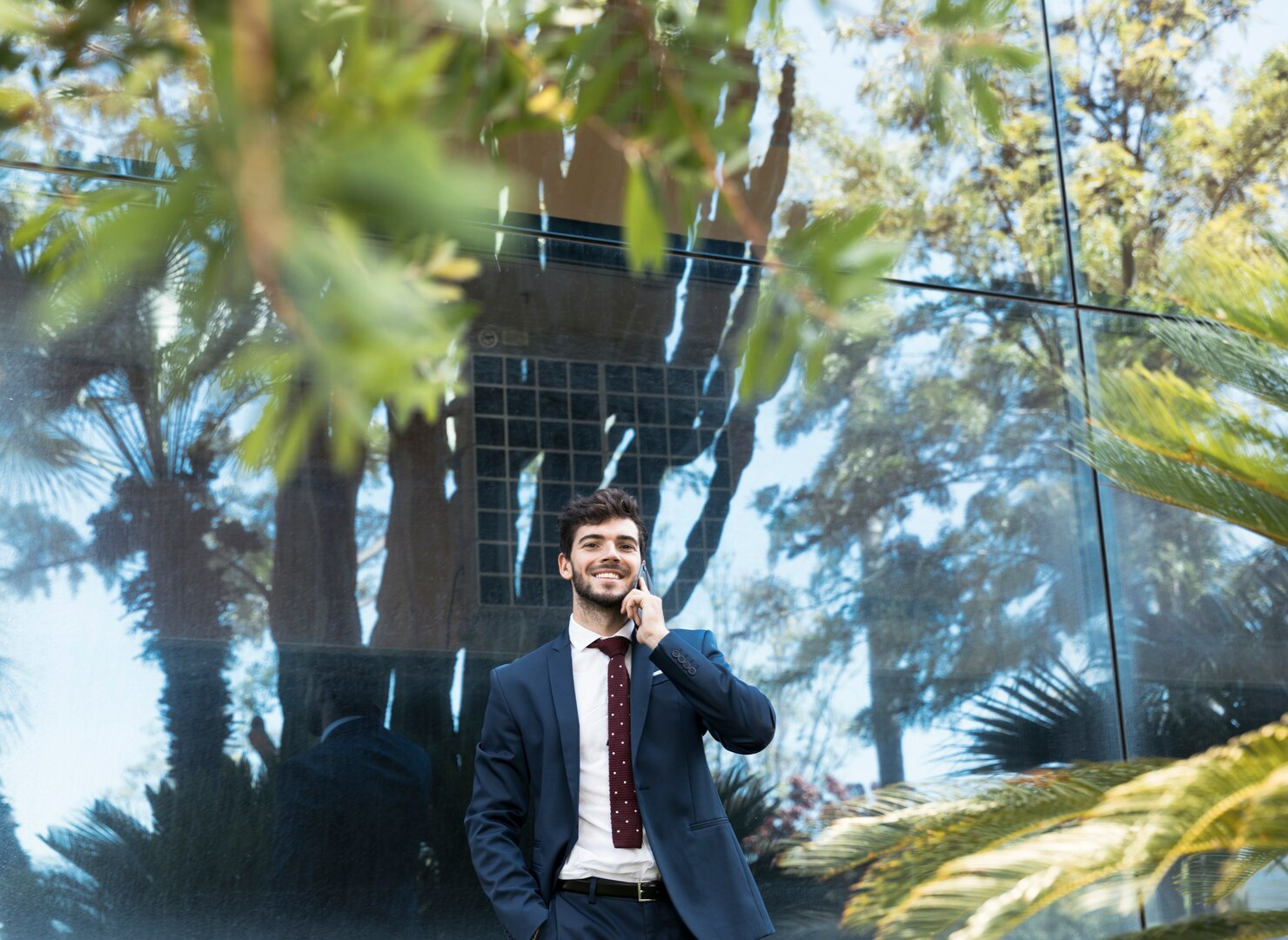 A business leader speaking on a phone outside a glass-fronted building.