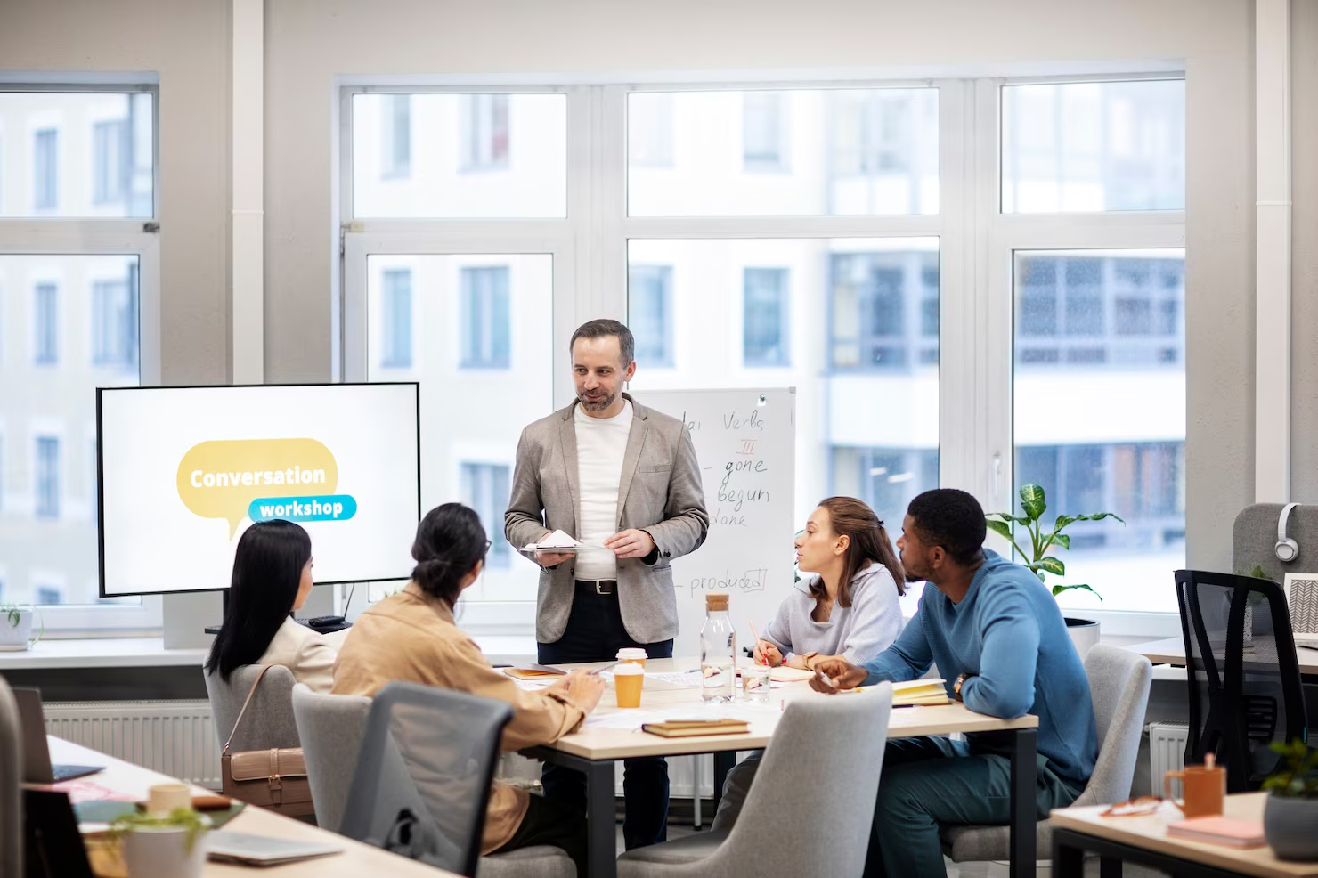 A facilitator leads a workplace workshop with colleagues gathered around a table.